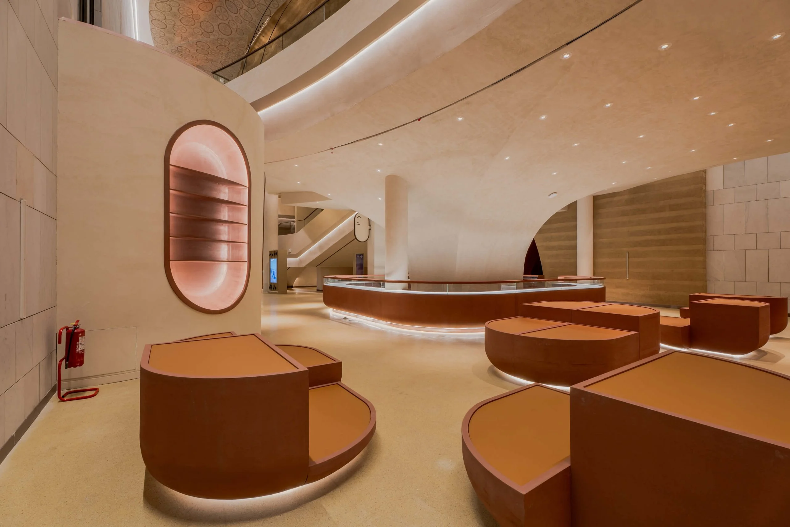Lobby with leather-clad display plinths, a curved glass counter and backlit oval niches in stone walls – King Fahad Cultural Center, Riyadh, Saudi Arabia, 2024 – architectural renovation