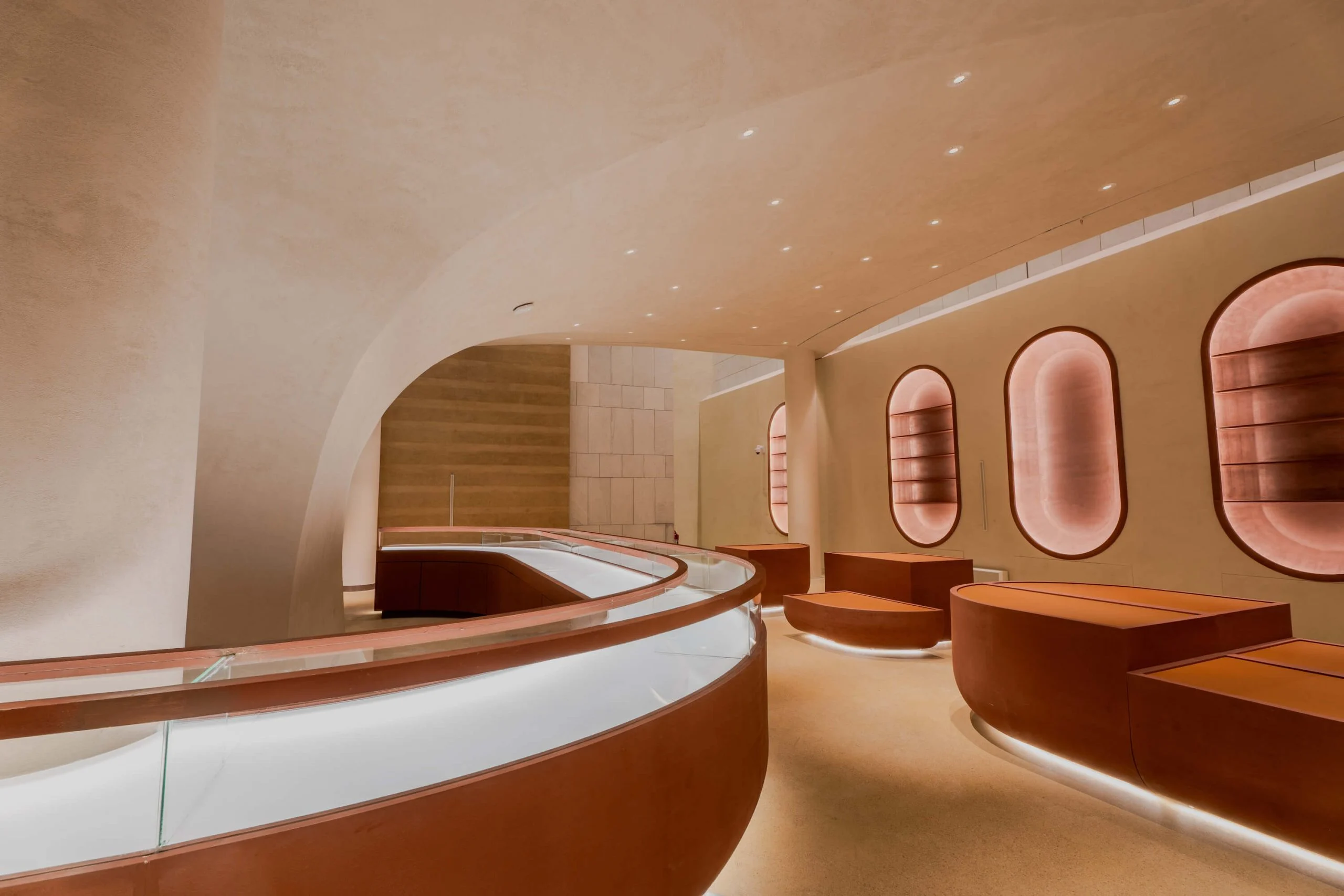 Curving glass display counter and leather-clad seating plinths beside a wall of glowing oval niches – King Fahad Cultural Center, Riyadh, Saudi Arabia, 2024 – architectural renovation