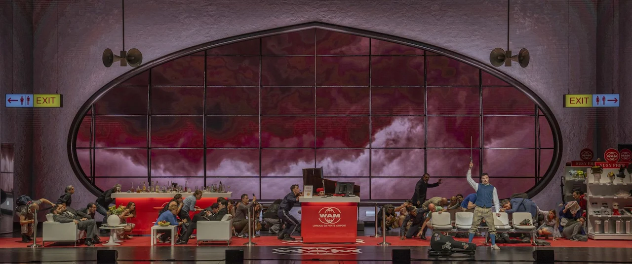 Airport set with the oval window filled by red clouds, passengers lounging around the check-in desk – Une Folle Journée Mozart Gala, Salzburg, Austria, 2024 – opera set design