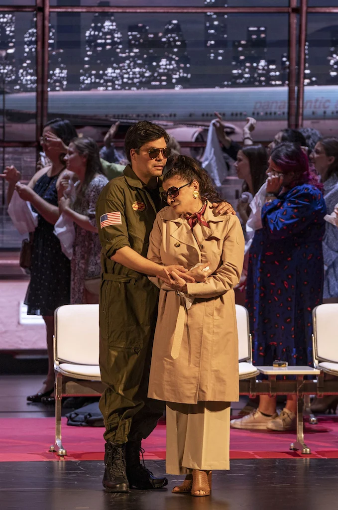Couple embracing in a pilot's flight suit and a trench coat among passengers in the terminal – Une Folle Journée Mozart Gala, Salzburg, Austria, 2024 – opera set design