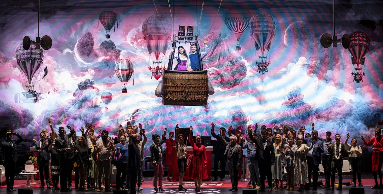 Finale with the cast cheering below a hot-air balloon and a pink and blue cloud projection – Une Folle Journée Mozart Gala, Salzburg, Austria, 2024 – opera set design
