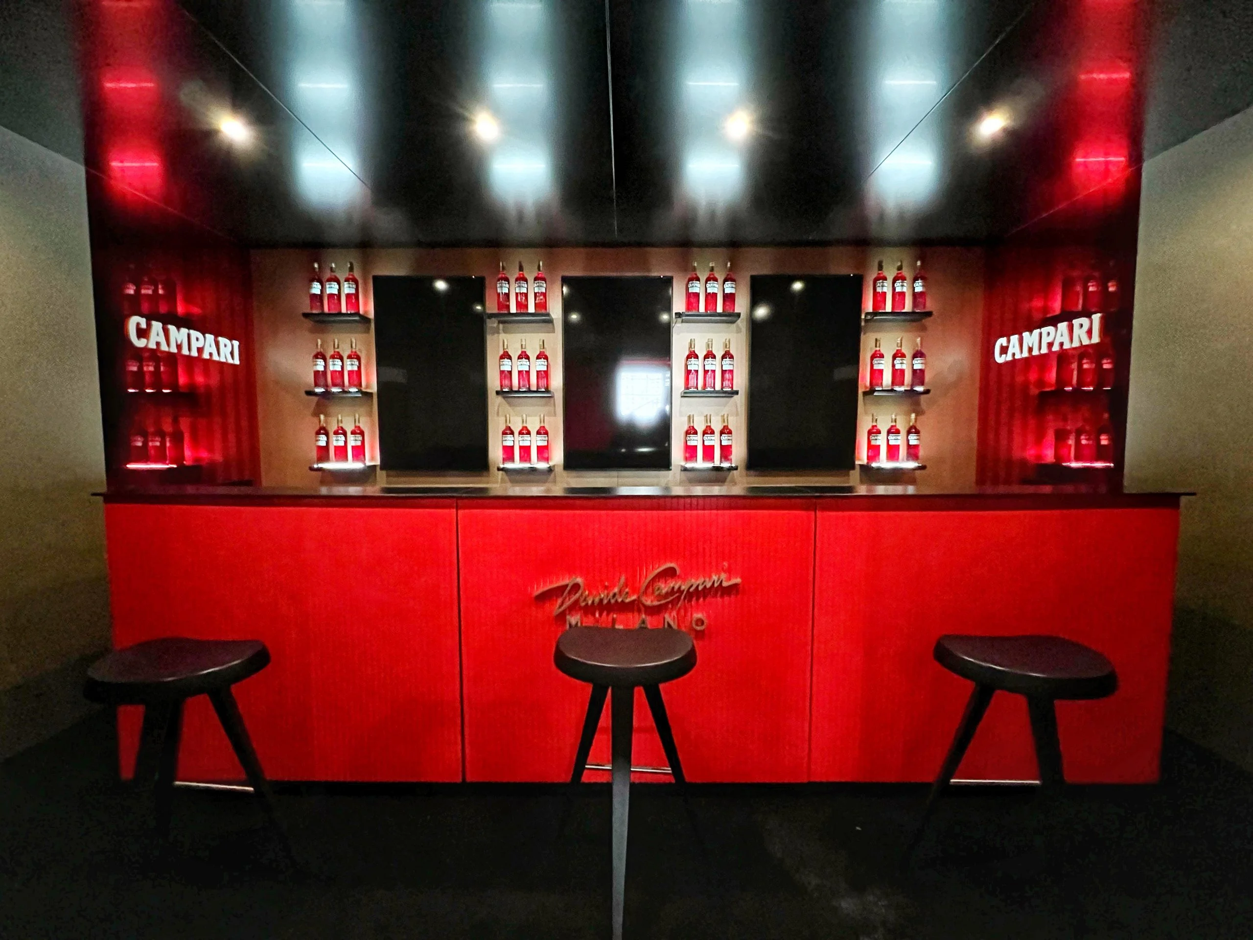 Red bar counter with Paolo Campari Milano lettering, three black stools and shelves of Campari bottles – Campari Cannes Film Festival 2024, France – event architecture