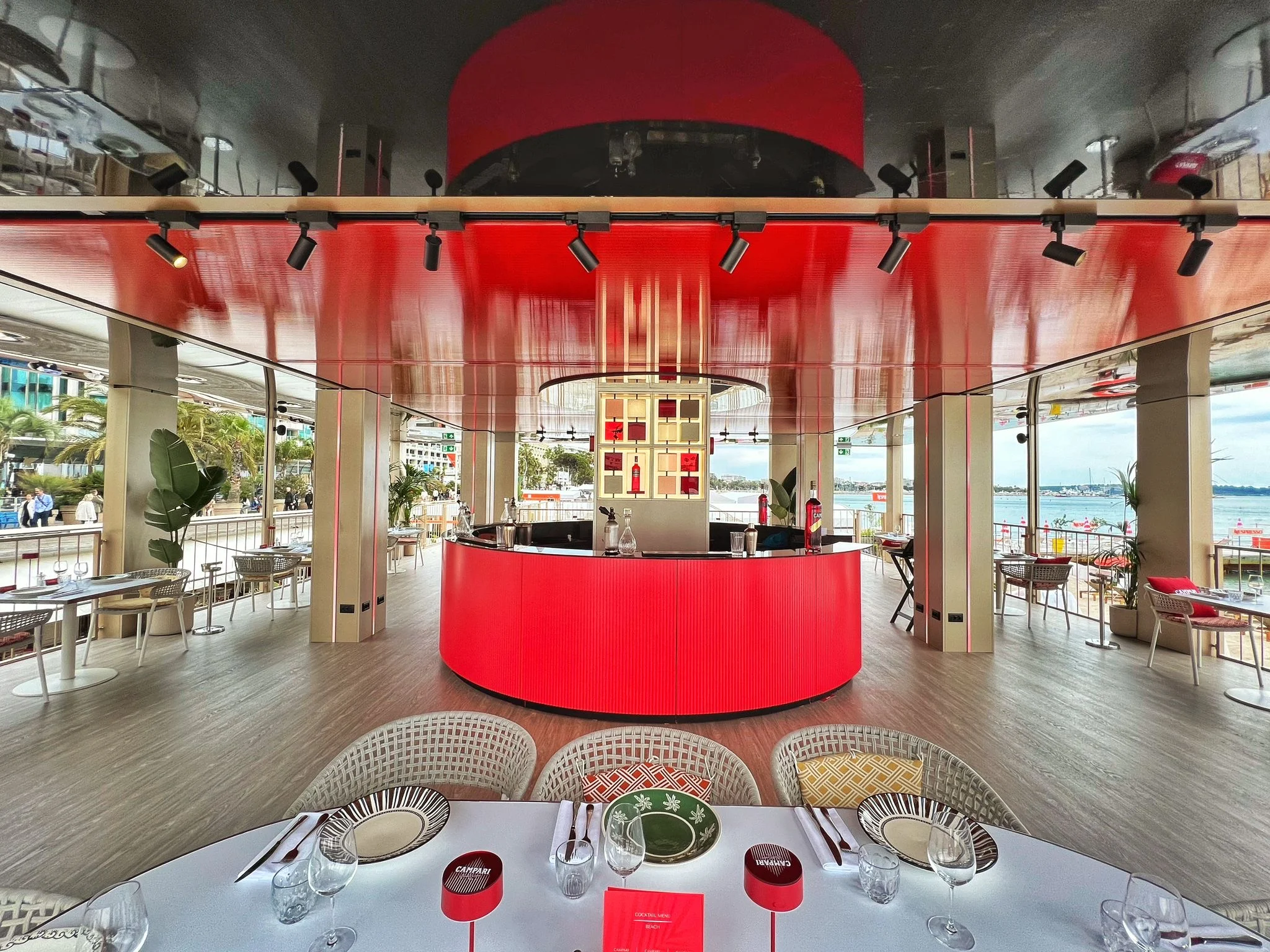 Terrace restaurant with a round red bar under a glossy red ceiling, laid tables in the foreground – Campari Cannes Film Festival 2024, France – event architecture