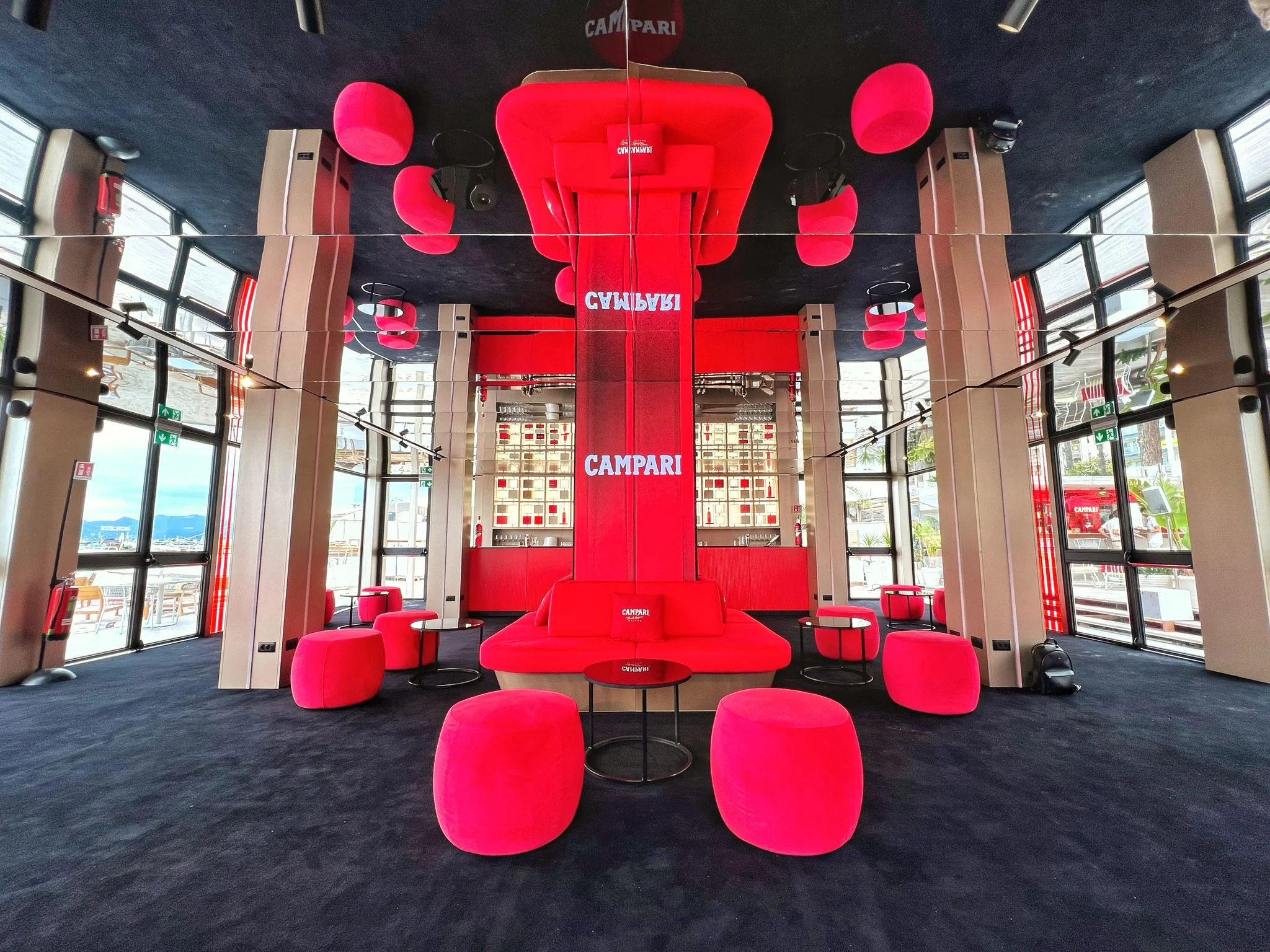 Dark lounge with a central red column, red poufs and sofas, and red cushions hanging from the mirrored ceiling – Campari Cannes Film Festival 2024, France – event architecture