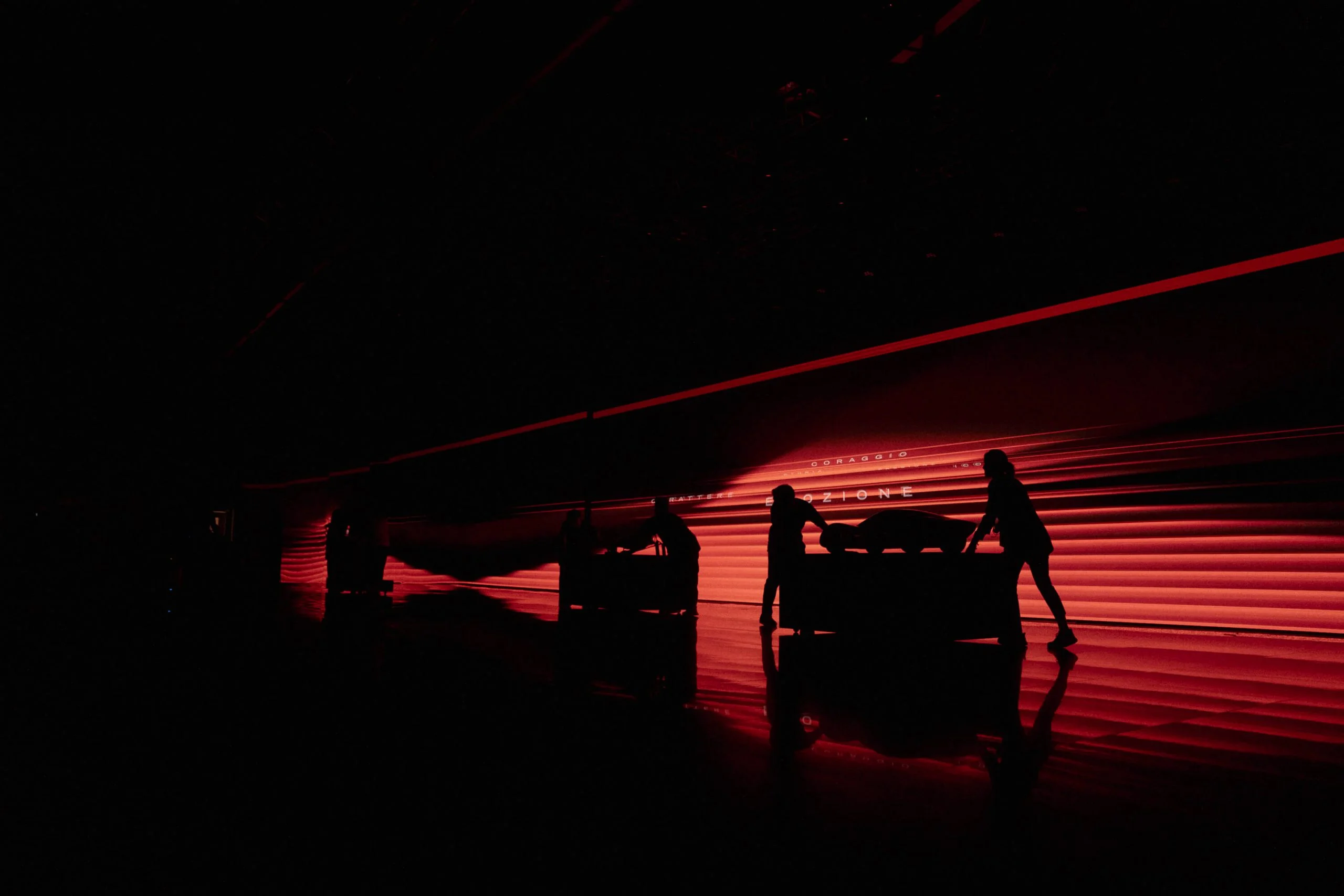 Silhouettes of crew pushing covered cars across a red-lit stage in front of a long LED wall – Alfa Romeo 33 Stradale Unveiling, Arese, Italy, 2023 – event design