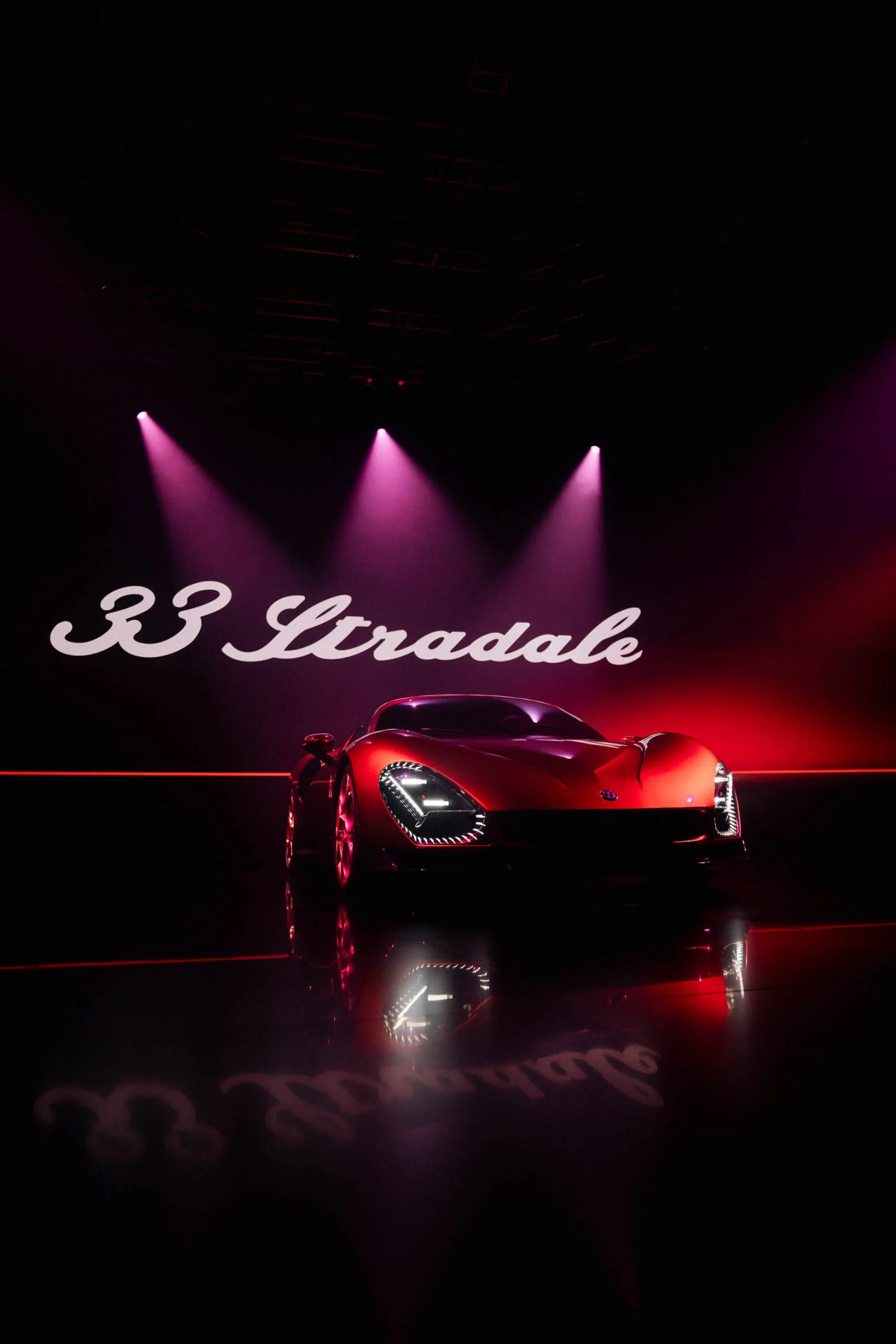 Red 33 Stradale under three pink spotlights, with the model name in white script on the wall behind – Alfa Romeo 33 Stradale Unveiling, Arese, Italy, 2023 – event design