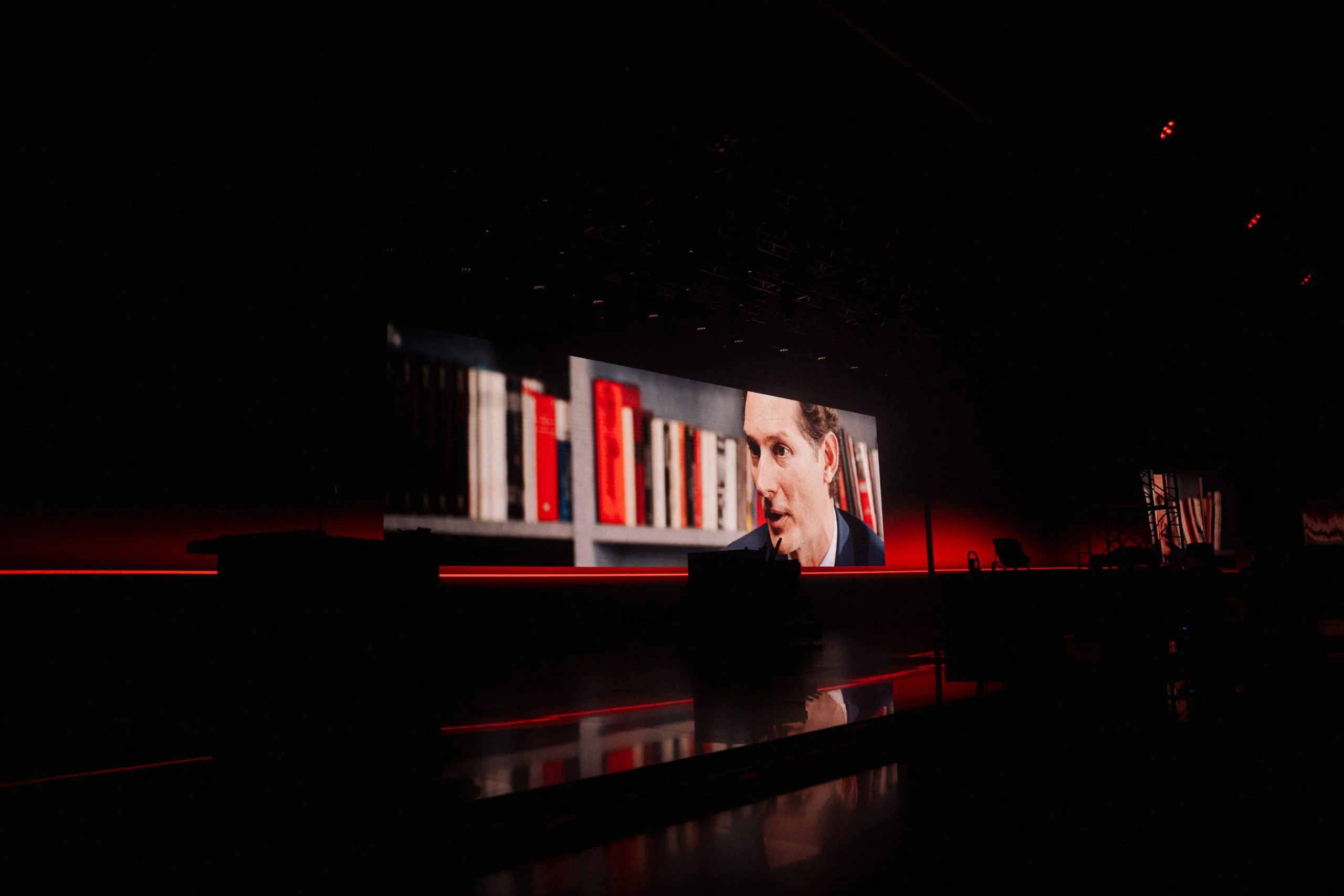 Dark stage with a long LED wall showing a speaker in front of a bookshelf – Alfa Romeo 33 Stradale Unveiling, Arese, Italy, 2023 – event design
