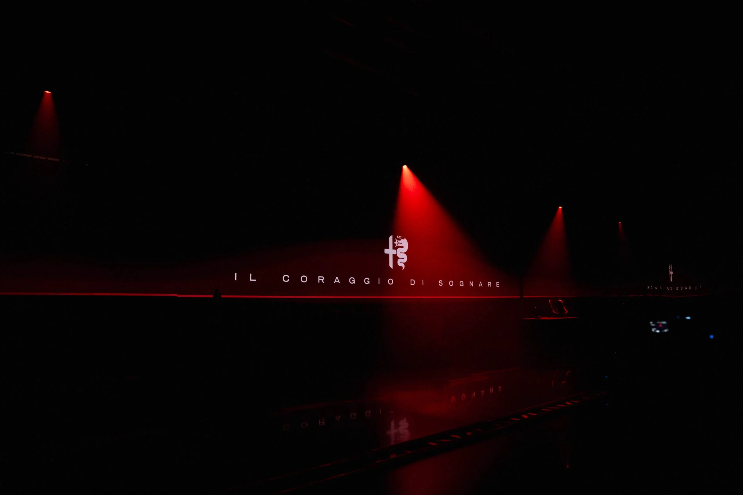 Alfa Romeo logo and the words Il Coraggio di Sognare on a dark wall under red spotlights – Alfa Romeo 33 Stradale Unveiling, Arese, Italy, 2023 – event design