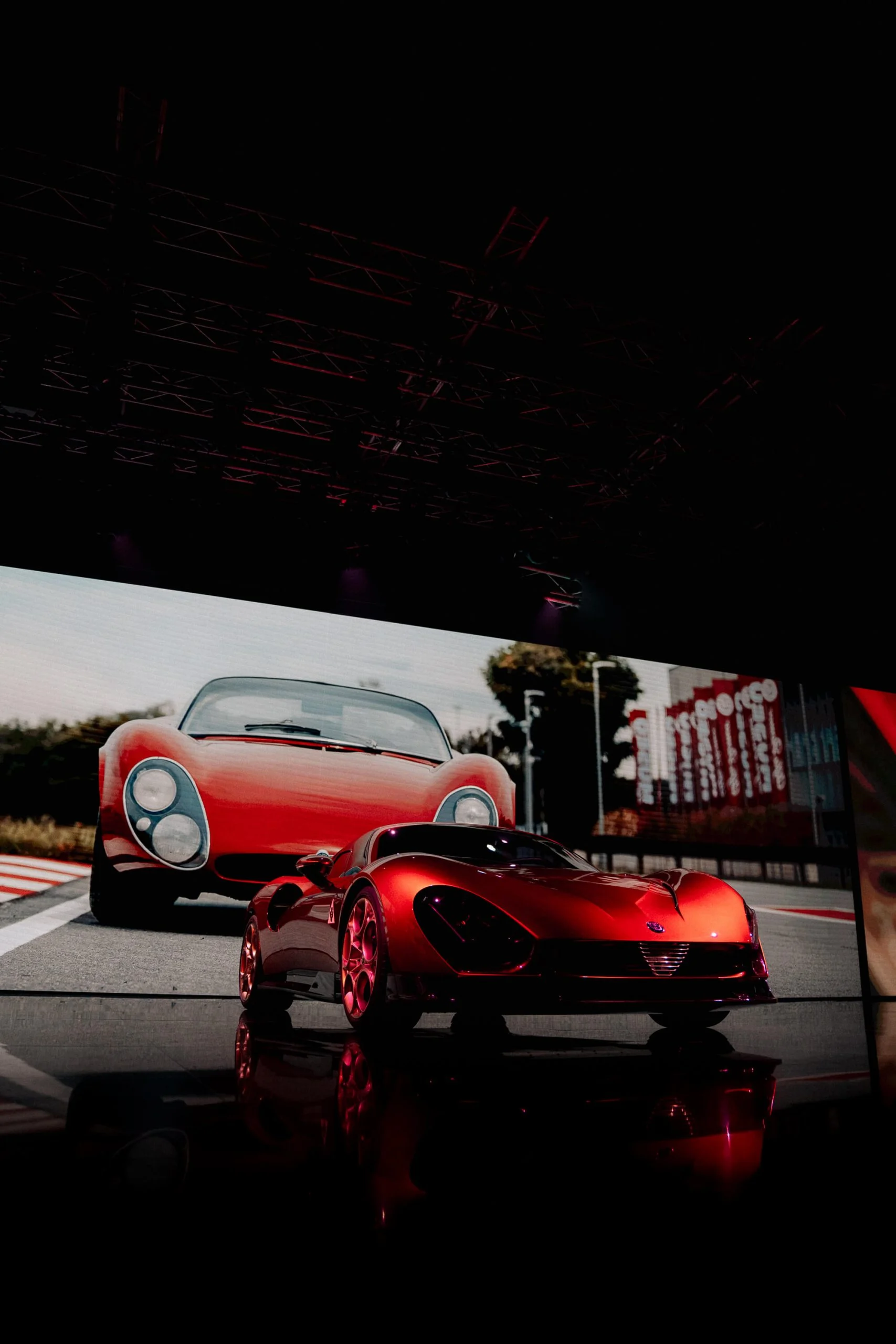 New 33 Stradale on stage before a giant screen showing the original 1960s car on a track – Alfa Romeo 33 Stradale Unveiling, Arese, Italy, 2023 – event design