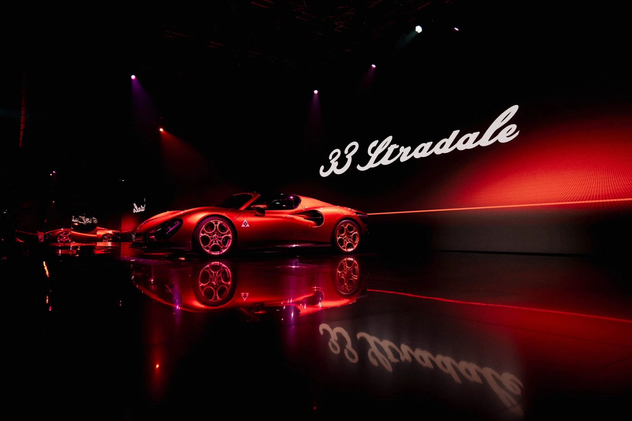 Red 33 Stradale with its name in white script on the wall, reflected on the black floor – Alfa Romeo 33 Stradale Unveiling, Arese, Italy, 2023 – event design