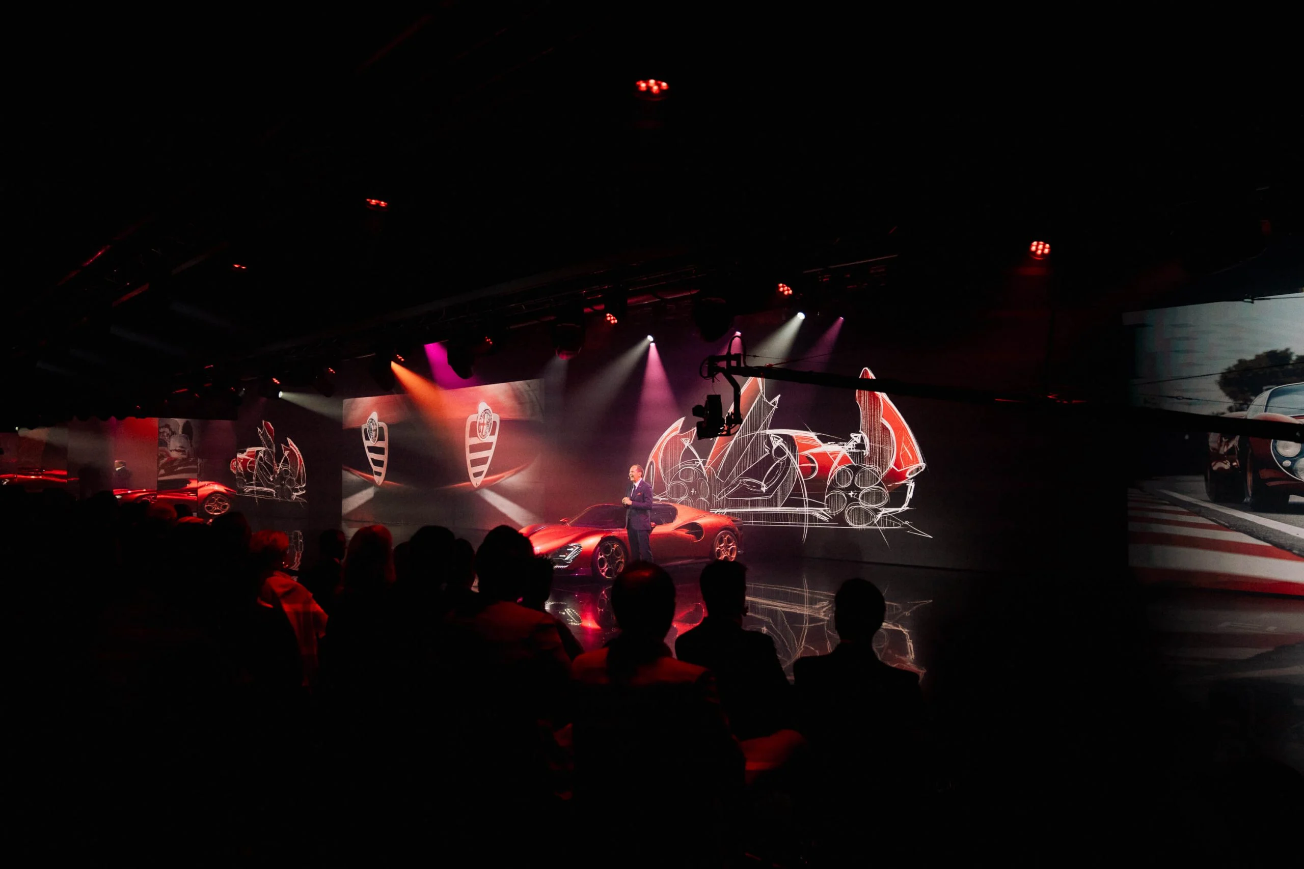 Presenter on stage beside the red car, with projected sketches of the 33 Stradale behind – Alfa Romeo 33 Stradale Unveiling, Arese, Italy, 2023 – event design