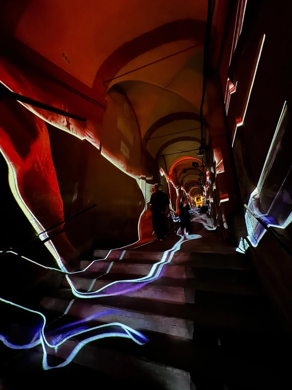 Portico steps traced by glowing blue light lines, red-lit walls and arches receding into the distance – Cesare Cremonini Festival dei Portici, Bologna, Italy, 2024 – event design