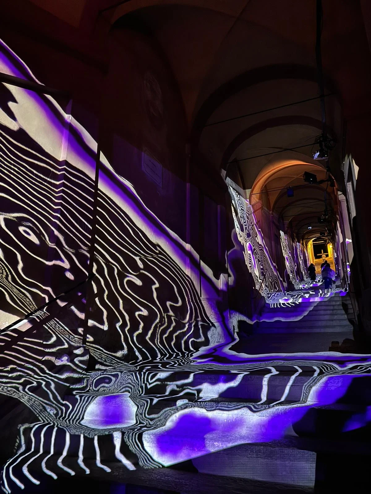 Black-and-white contour-line projections with purple patches flowing over the portico walls and stairs – Cesare Cremonini Festival dei Portici, Bologna, Italy, 2024 – event design