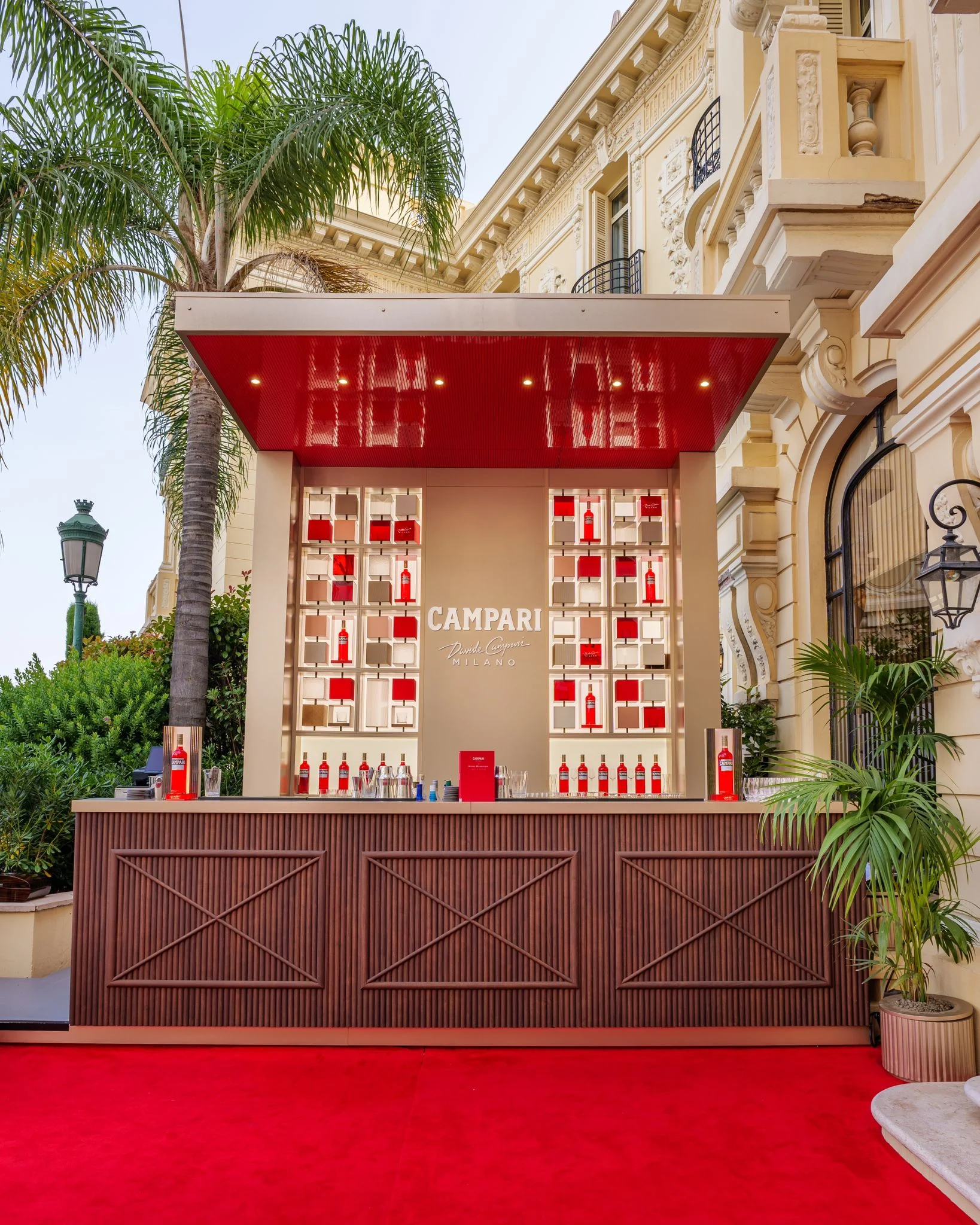 Campari pop-up bar with a glossy red canopy, red carpet and bottle shelves beside the Belle Epoque hotel facade – Campari Pop-Up Bar at the Hôtel Hermitage, Monte Carlo, Monaco, 2024 – hospitality design