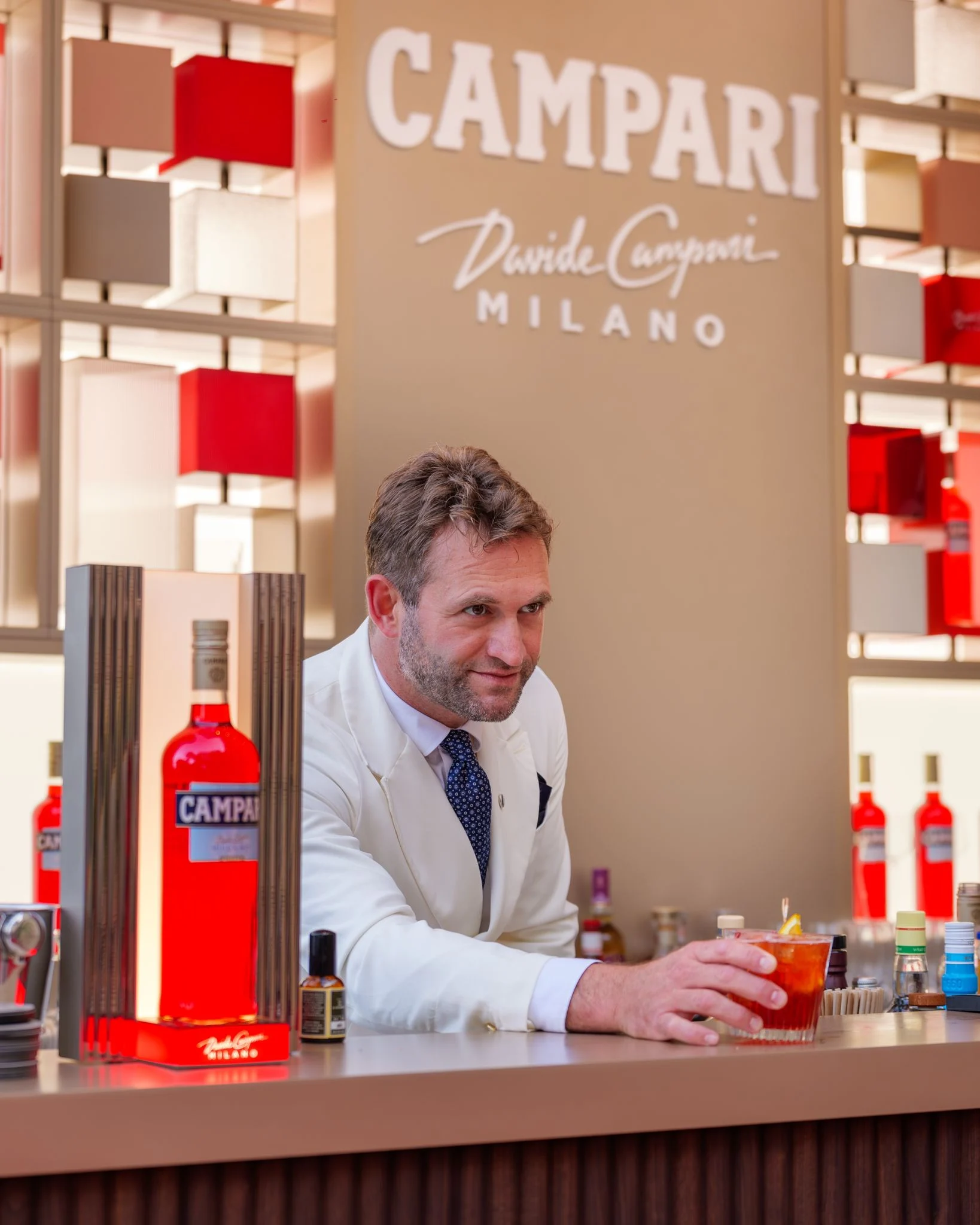 Bartender in a white jacket serving a cocktail at the Campari counter, red bottles on display – Campari Pop-Up Bar at the Hôtel Hermitage, Monte Carlo, Monaco, 2024 – hospitality design