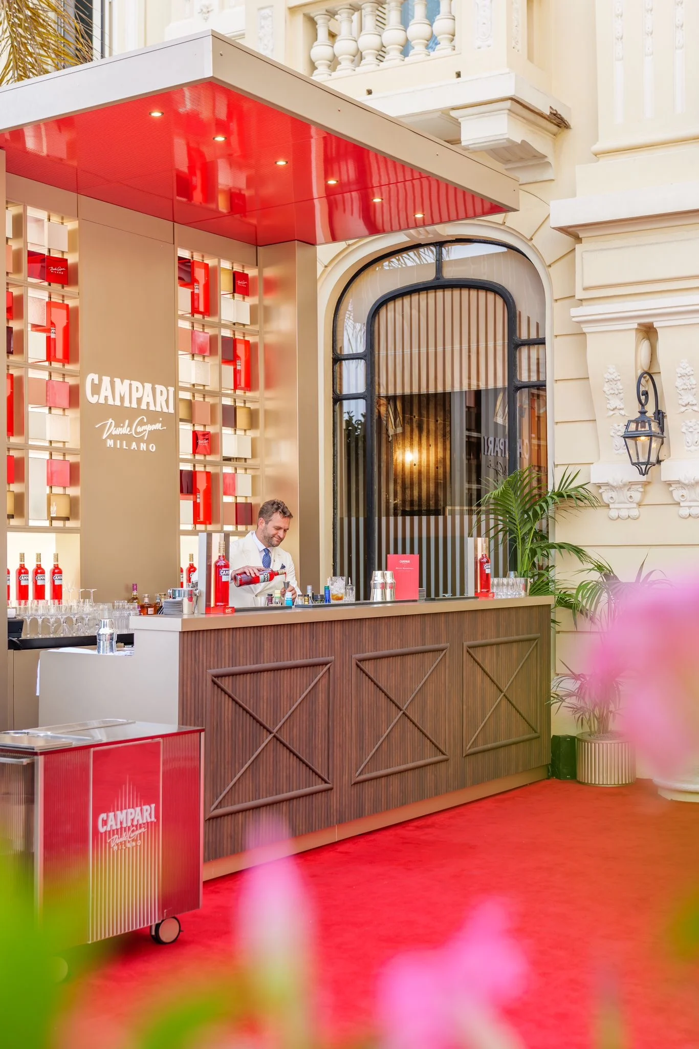 Side view of the Campari bar and a red trolley on the red carpet, with the hotel's arched window – Campari Pop-Up Bar at the Hôtel Hermitage, Monte Carlo, Monaco, 2024 – hospitality design