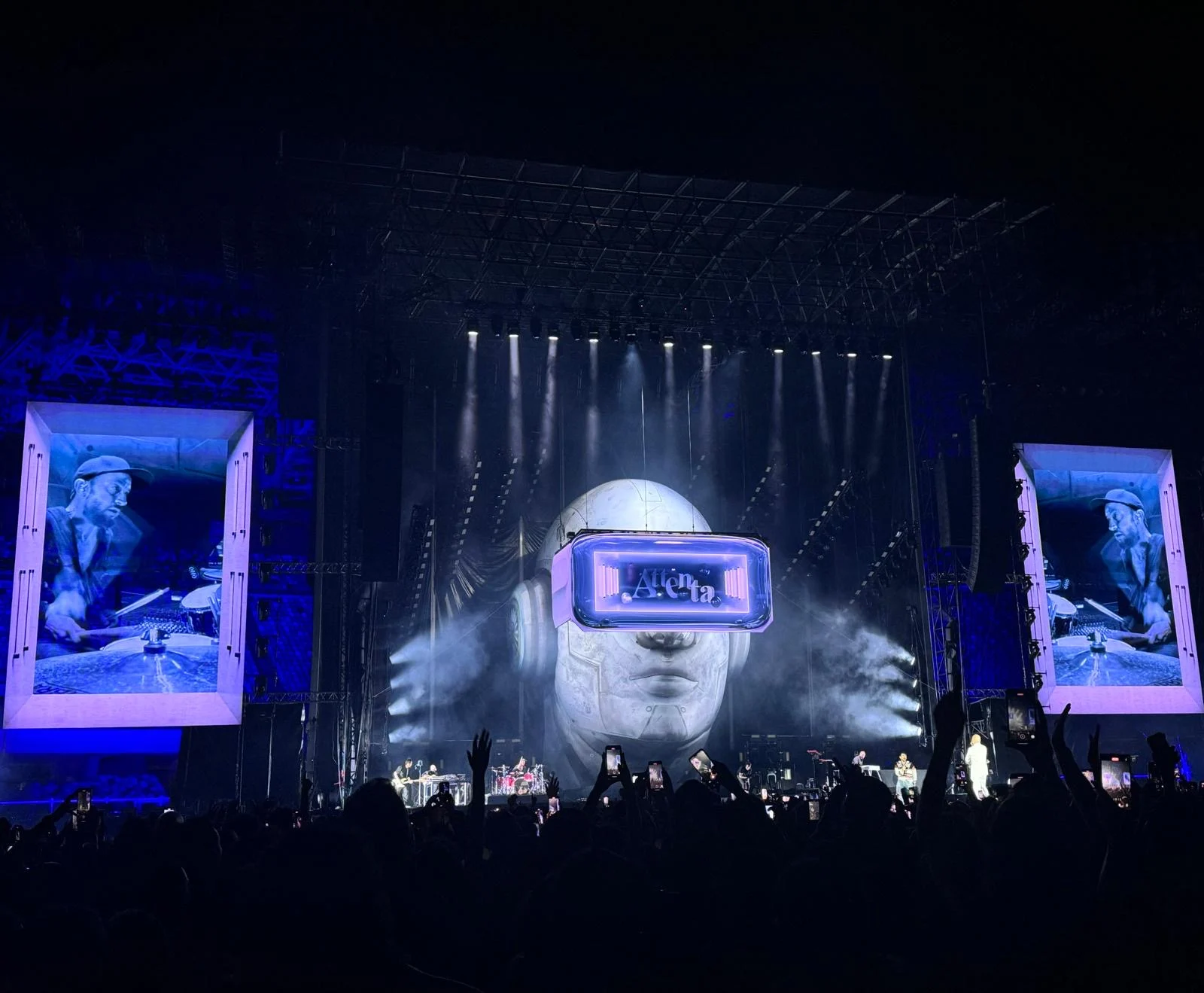Wide view of the stadium stage with the giant visored head, framed side screens and raised phones – Negramaro Stadi 2024, Italy – concert stage design