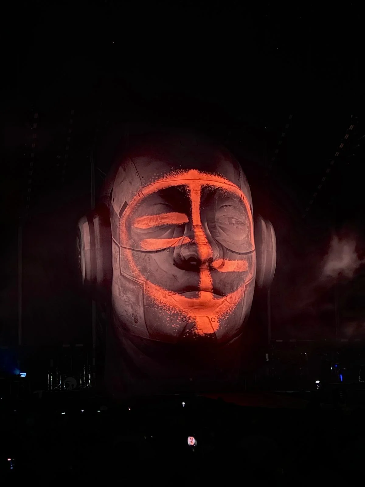 Giant head sculpture in darkness, with orange video mapping tracing lines on its face – Negramaro Stadi 2024, Italy – concert stage design