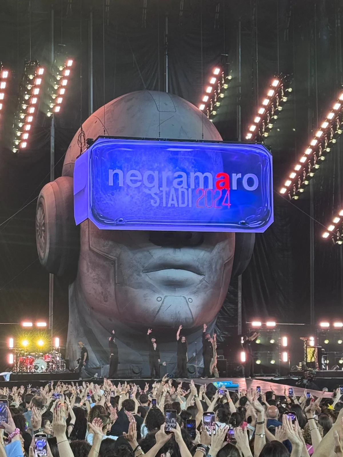 Giant head with headphones and an LED visor reading negramaro Stadi 2024, the band on stage below – Negramaro Stadi 2024, Italy – concert stage design