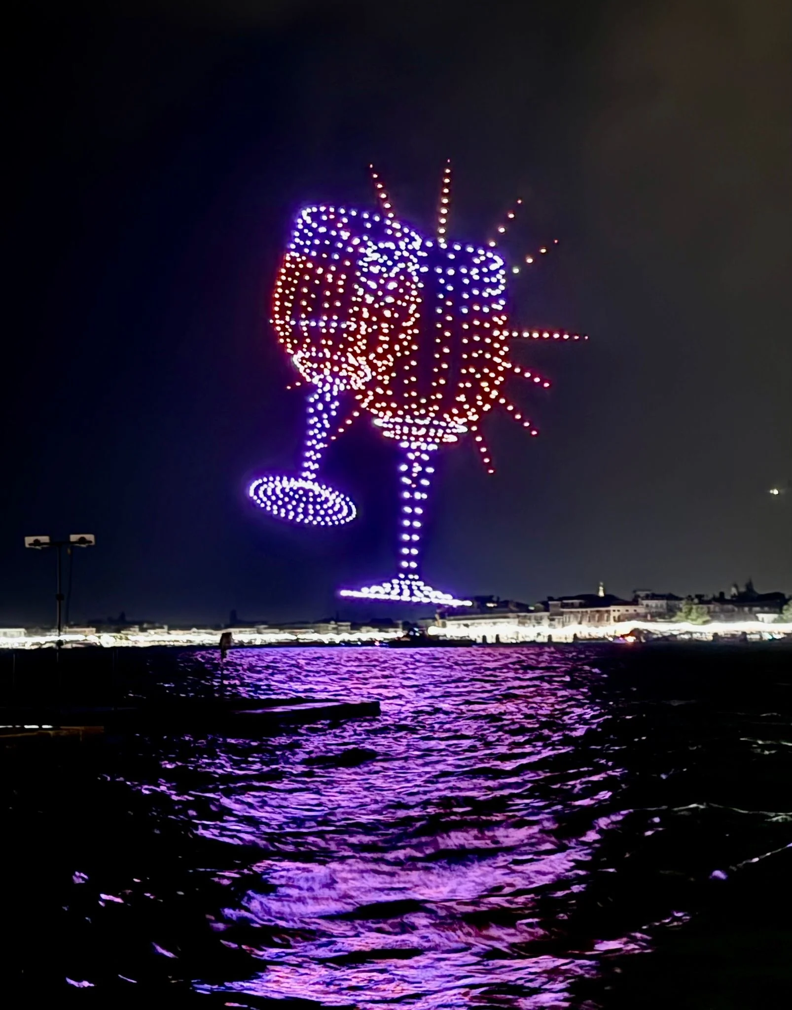 Two toasting glasses drawn by drones in the night sky, with a burst of light around them – Aperol Redentore Drone Show, Venice, Italy, 2024 – creative direction