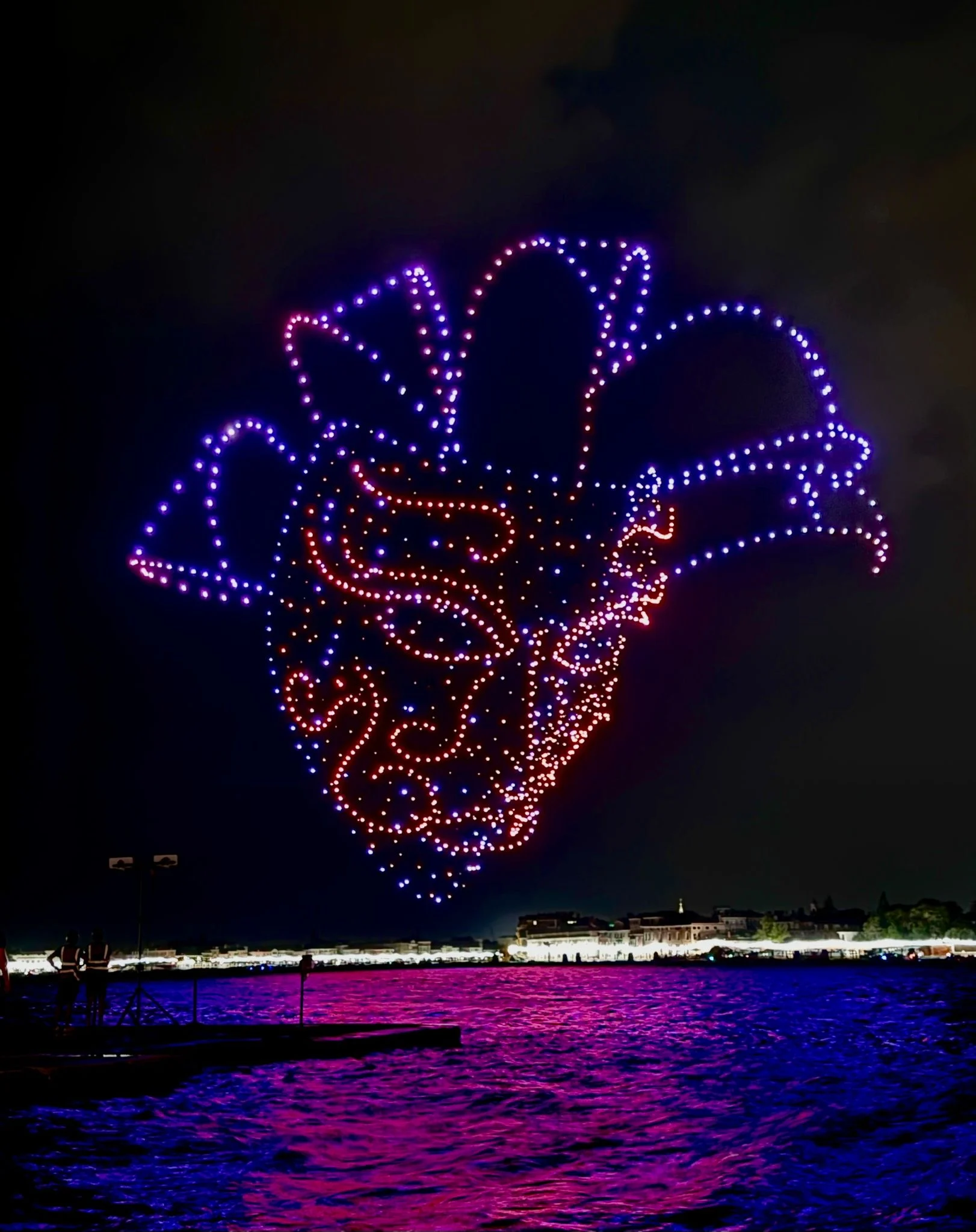 Drone formation of a Venetian Carnival mask in purple and orange lights above the lagoon – Aperol Redentore Drone Show, Venice, Italy, 2024 – creative direction