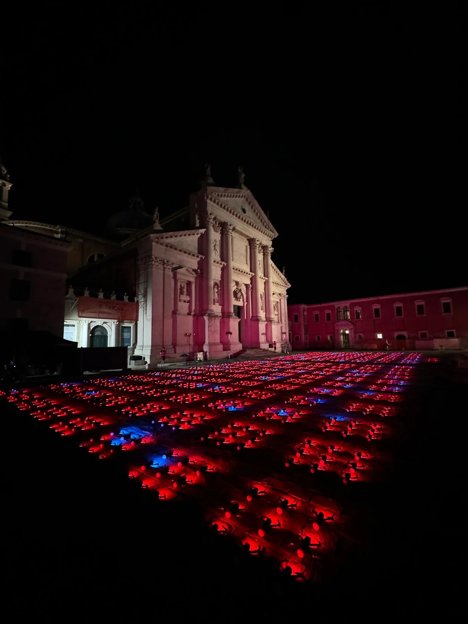 Rows of drones glowing red and blue on the ground before an illuminated church façade at night – Aperol Redentore Drone Show, Venice, Italy, 2024 – creative direction