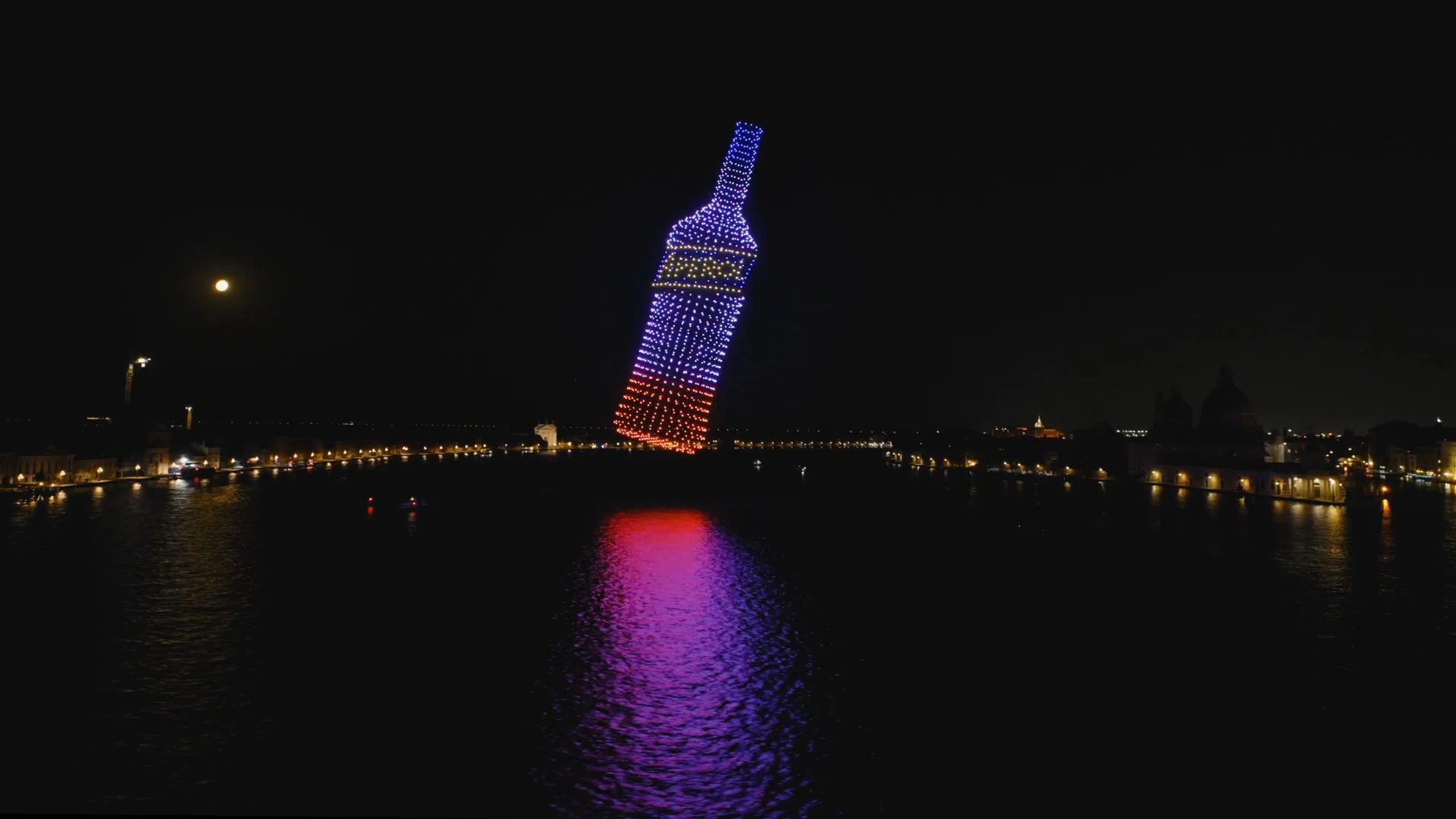 Aerial night view of drones forming a giant Aperol bottle over the Bacino di San Marco, reflected in the water – Aperol Redentore Drone Show, Venice, Italy, 2024 – creative direction