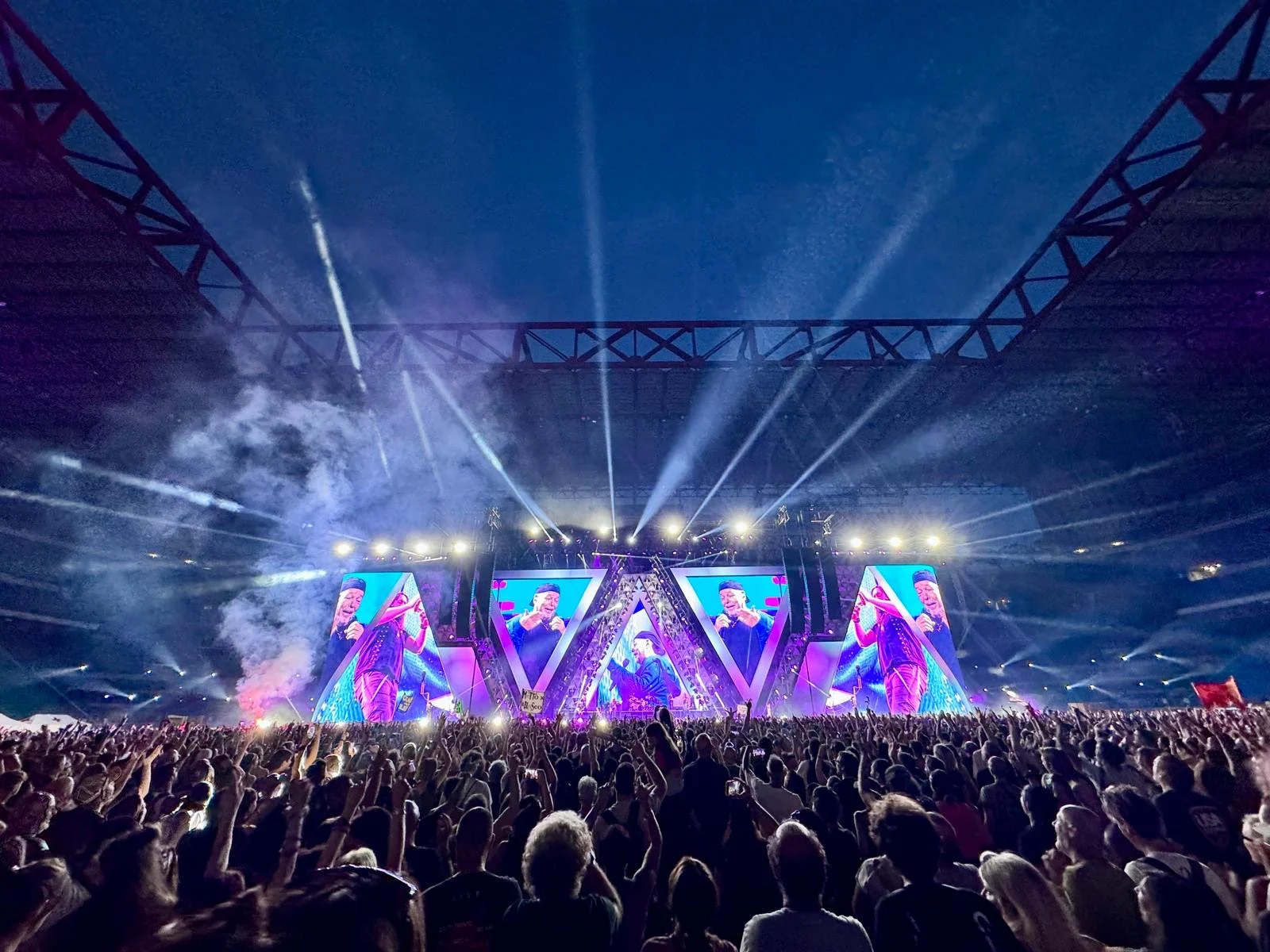 Night view of the stage with triangular maxi-screens, light beams and smoke rising over the packed stadium – Vasco Rossi Live 2024, Italy – concert stage design