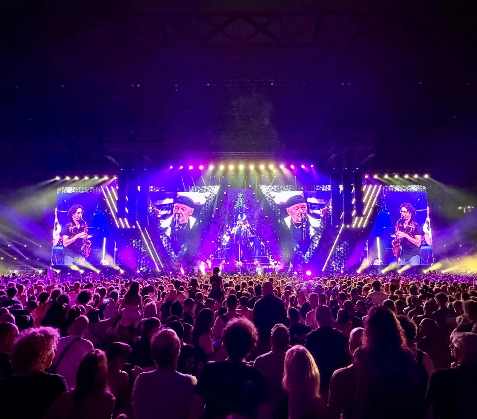 Stage bathed in purple light, screens showing a saxophonist and the singer while the crowd watches – Vasco Rossi Live 2024, Italy – concert stage design