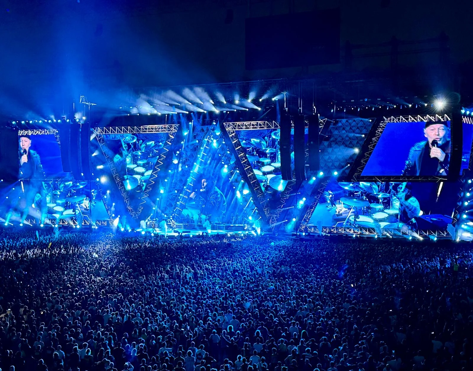 Stage and crowd in deep blue light, angular truss frames and screens close-up on the singer – Vasco Rossi Live 2024, Italy – concert stage design