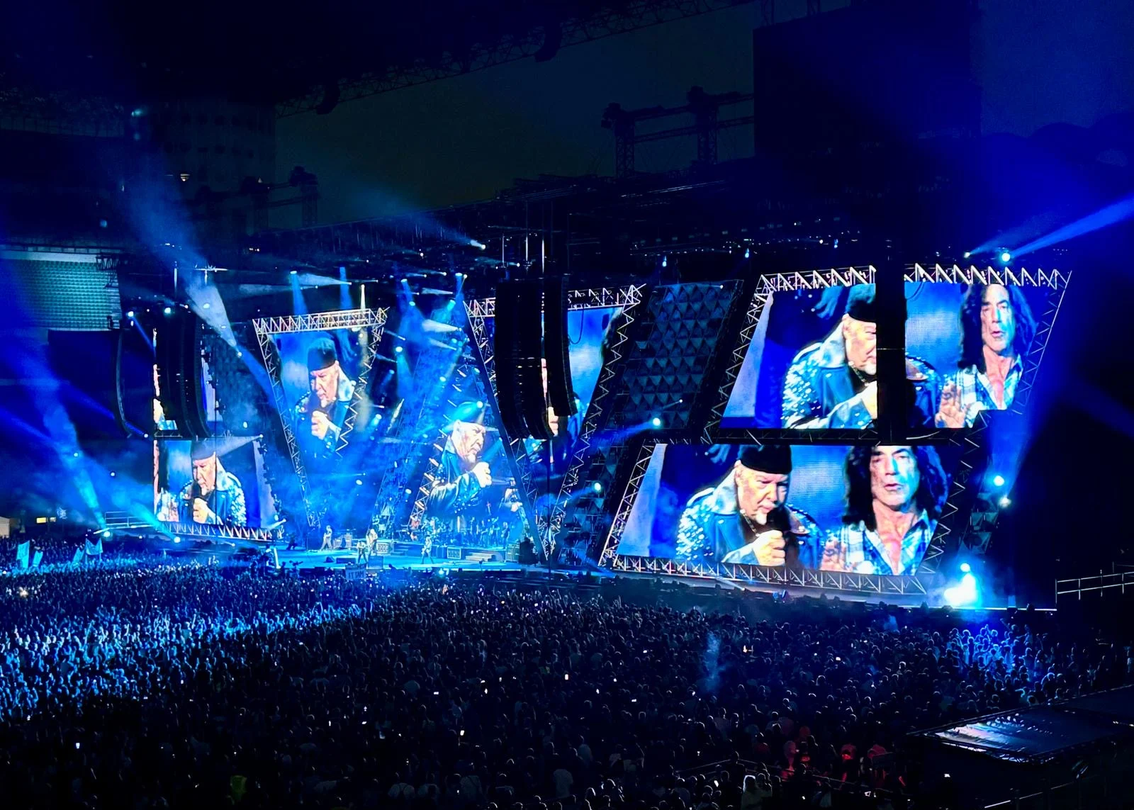 Side view of the stage in blue light, angular screen frames showing the singer and a guitarist – Vasco Rossi Live 2024, Italy – concert stage design