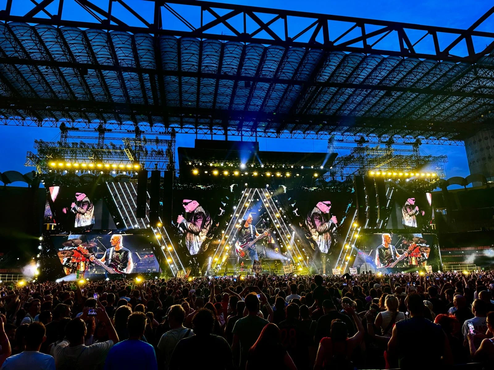 Vasco Live 2024 stage at dusk under the stadium roof, triangular LED screens showing the band above the crowd – Vasco Rossi Live 2024, Italy – concert stage design