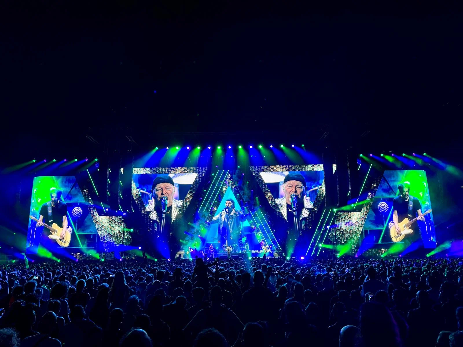 Stage glowing in green and blue, screens showing the singer and guitarists in angular frames – Vasco Rossi Live 2024, Italy – concert stage design