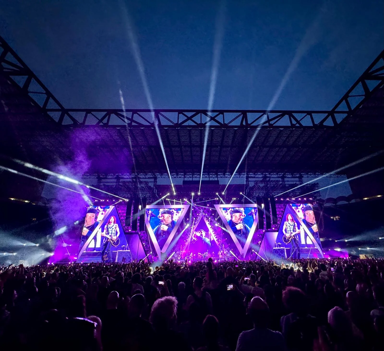 Purple-lit stage with searchlight beams sweeping the night sky and smoke drifting over the crowd – Vasco Rossi Live 2024, Italy – concert stage design
