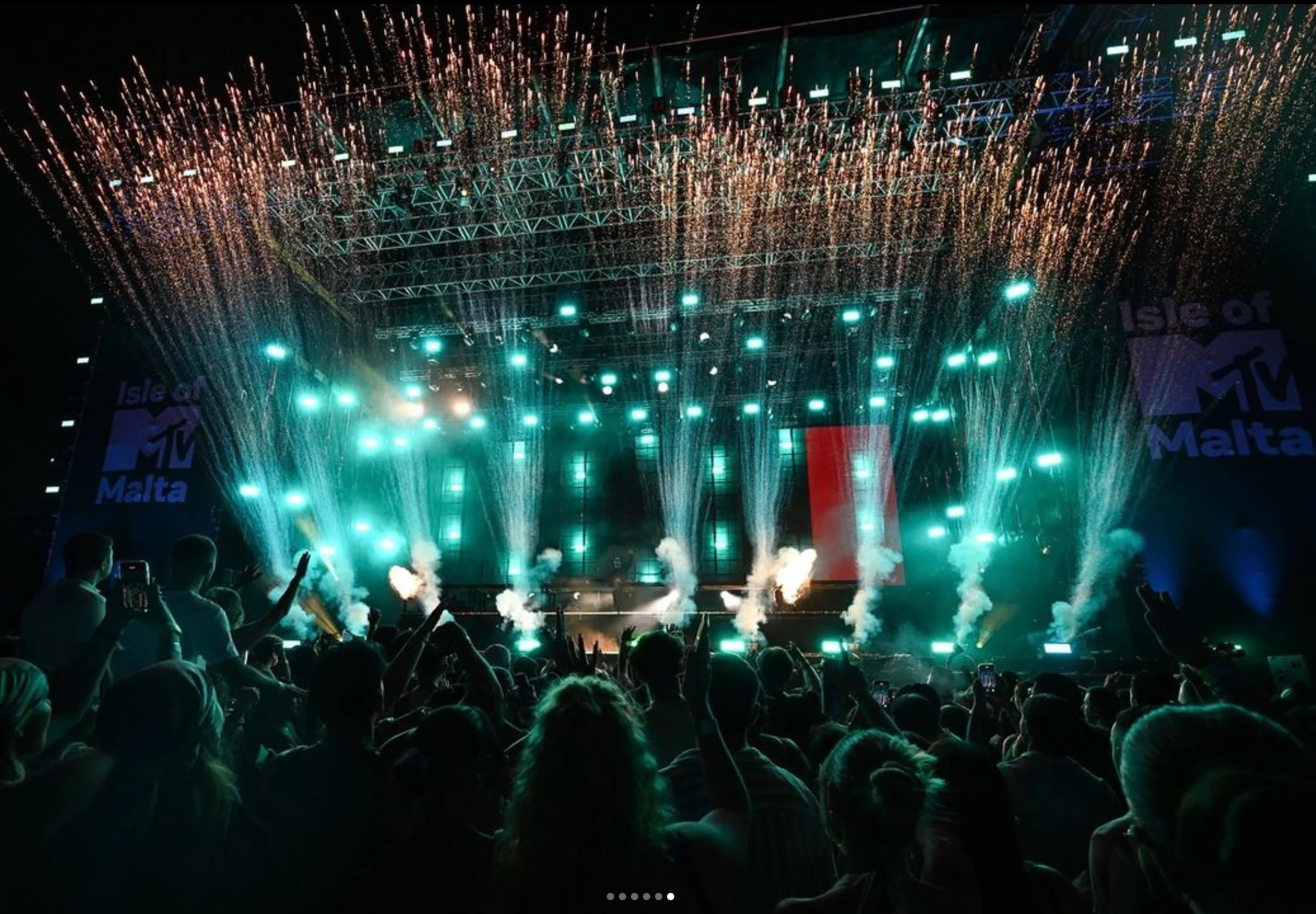 Isle of MTV Malta stage at night: teal lights and cascades of sparks over a crowd with raised hands – Isle of MTV 2024, Floriana, Malta – concert stage design