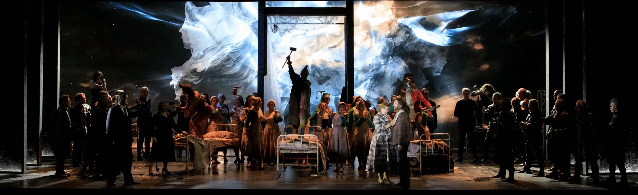 Chorus around hospital beds on a dark stage, with a projected icy white storm filling the backdrop – Il Trovatore at Teatro Comunale Nouveau, Bologna, Italy, 2024 – opera set design