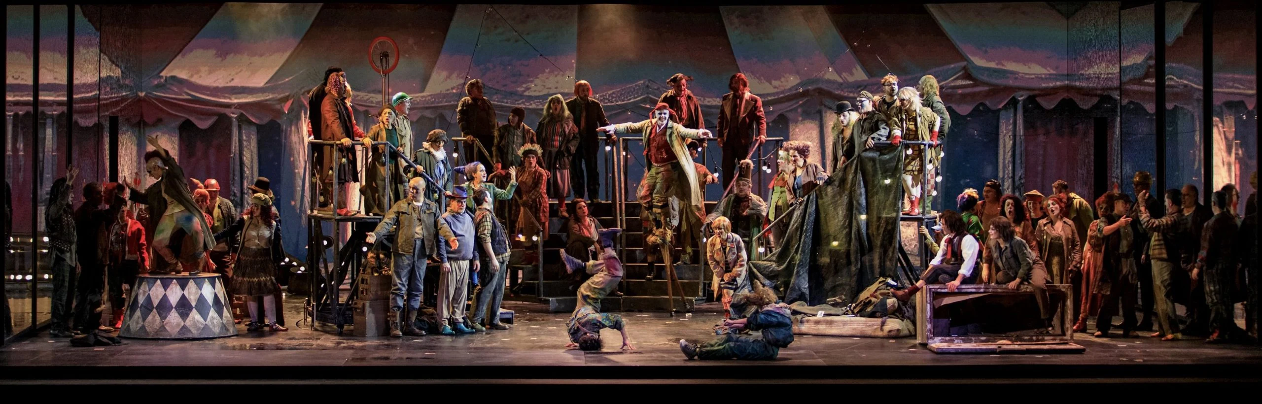 Il Trovatore staging: a crowded circus scene with performers on metal stairs under a faded big-top tent – Il Trovatore at Teatro Comunale Nouveau, Bologna, Italy, 2024 – opera set design