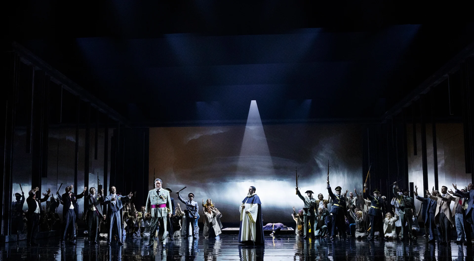 Ensemble in uniforms with raised rifles flanking a cleric, a beam of light on a cloudy projected backdrop – Don Carlo at the Royal Danish Theatre, Copenhagen, Denmark, 2024 – opera set design