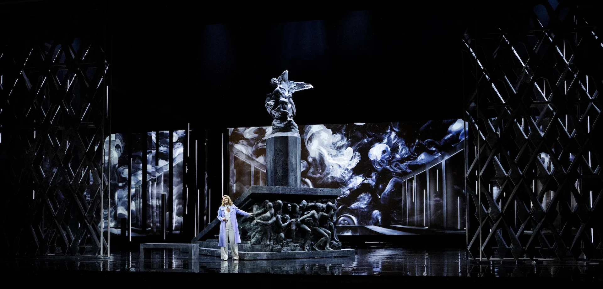 Singer in white before a monument topped by a winged statue, monochrome projections and lattice towers – Don Carlo at the Royal Danish Theatre, Copenhagen, Denmark, 2024 – opera set design