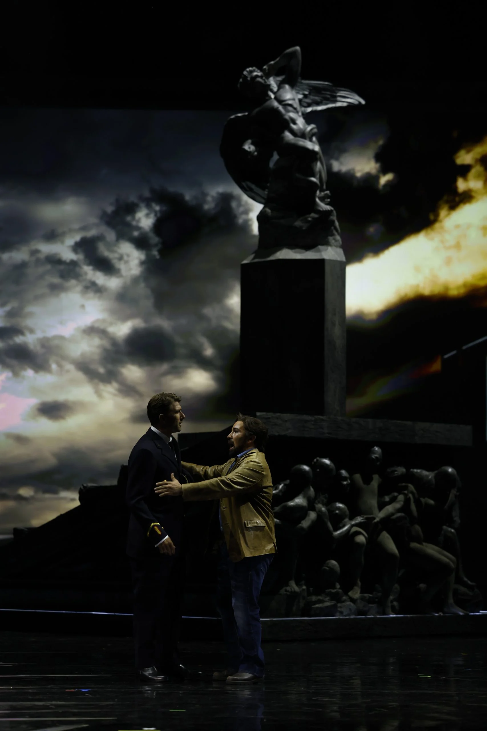 Two men facing each other below the winged-statue monument against a stormy sky projection – Don Carlo at the Royal Danish Theatre, Copenhagen, Denmark, 2024 – opera set design