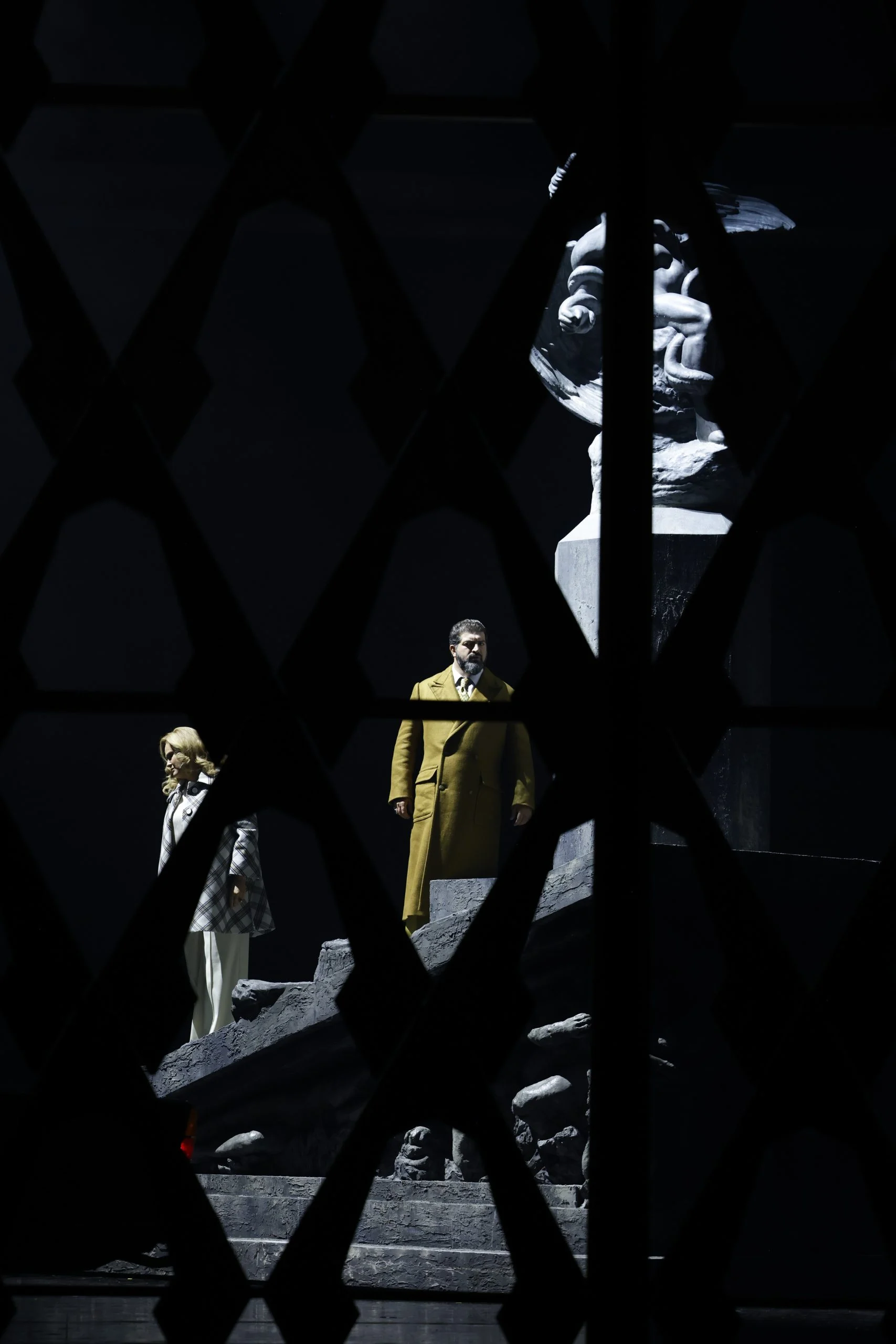 Two singers on the monument steps seen through a dark diamond lattice in the foreground – Don Carlo at the Royal Danish Theatre, Copenhagen, Denmark, 2024 – opera set design