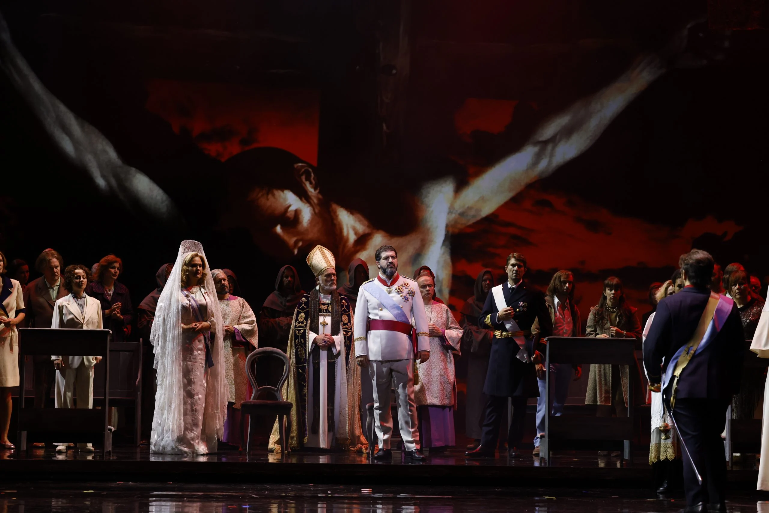 Bride in a white veil, a bishop, an officer in white uniform and chorus before a giant projected crucifix – Don Carlo at the Royal Danish Theatre, Copenhagen, Denmark, 2024 – opera set design