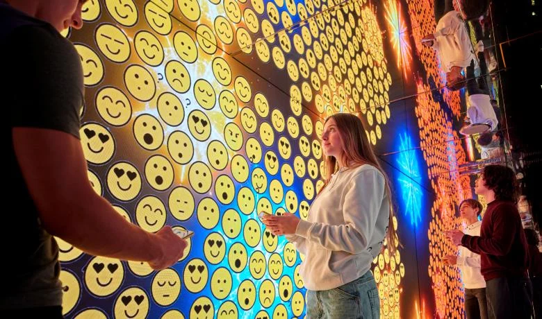Visitor in a mirrored room surrounded by walls of glowing emoji faces – STEP FuturAbility District by Fastweb, Milan, Italy, 2022 – exhibition design