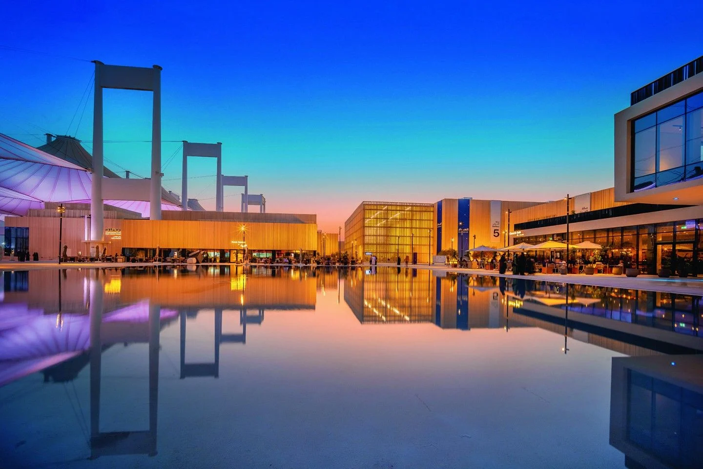 Biennale site at dusk under a blue and orange sky, pavilions and tent pylons reflected in a long pool – Islamic Arts Biennale, Jeddah, Saudi Arabia, 2023 – architecture