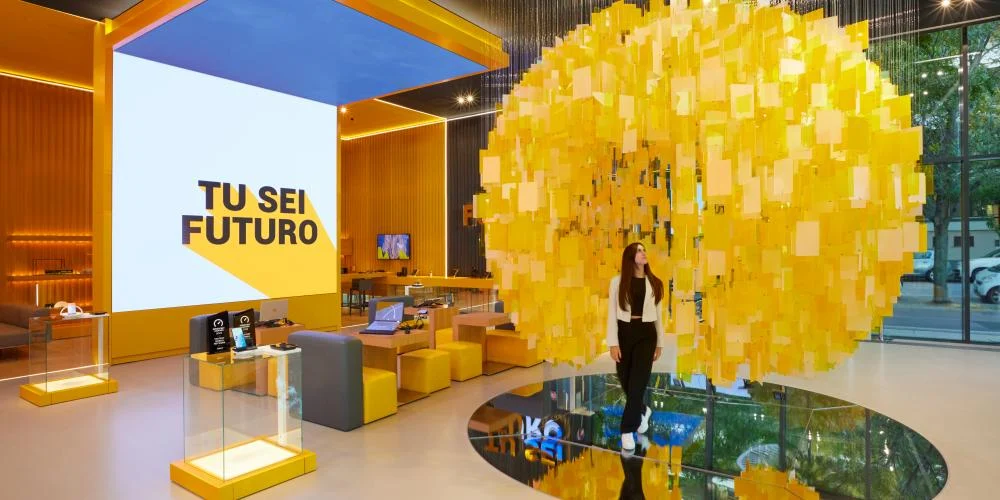Visitor standing beneath the suspended sphere of yellow tiles, reflected in a round mirror set in the floor – STEP FuturAbility District by Fastweb, Milan, Italy, 2022 – exhibition design