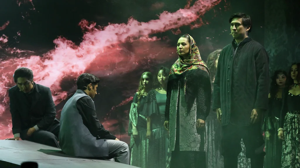 Performers in traditional dress before a projection of red smoke, two men seated at the stage edge – Waltz Karoly at Turkistan Theatre, Kazakhstan, 2024 – set design