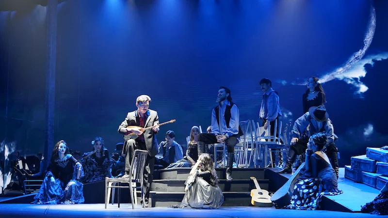 Blue night scene with a crescent moon projection, a mandolin player seated among the ensemble on steps – Waltz Karoly at Turkistan Theatre, Kazakhstan, 2024 – set design