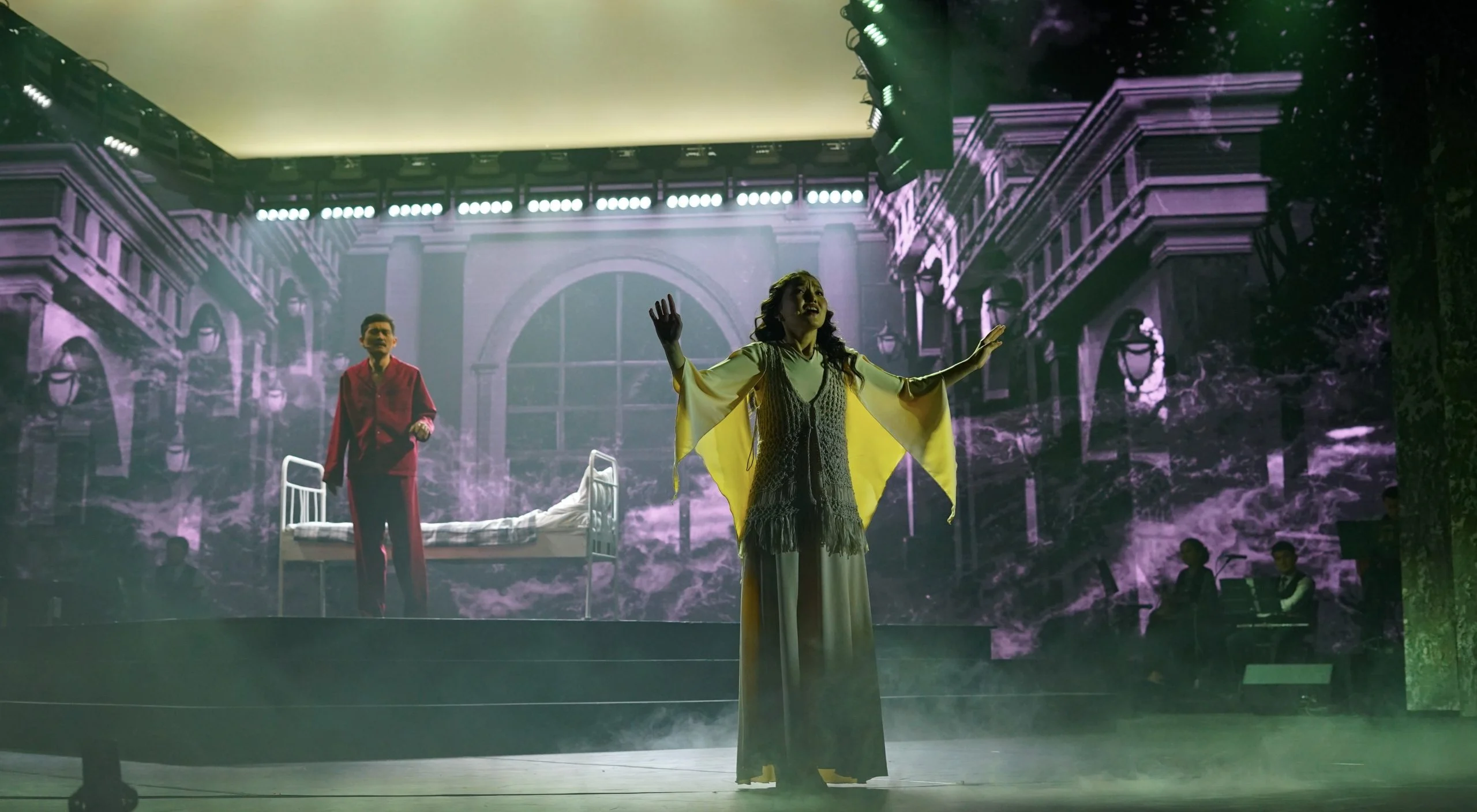 Singer in a yellow cape centre stage, a hospital bed behind and projected palace facades all around – Waltz Karoly at Turkistan Theatre, Kazakhstan, 2024 – set design