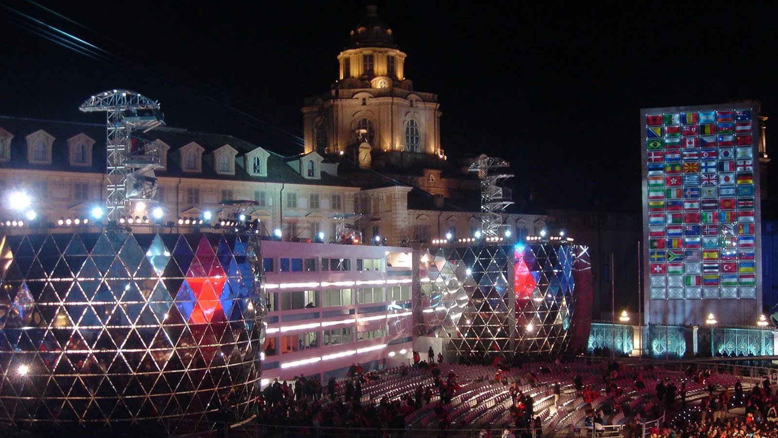 Night view of Piazza Castello with geodesic light pavilions, a wall of flags and the domed church behind – Medals Plaza, Turin 2006 Winter Olympics, Italy – event design