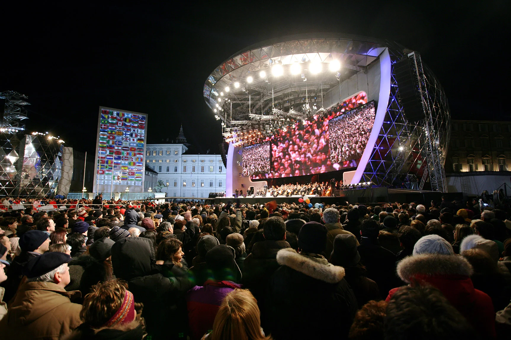 Medals Plaza in Piazza Castello at night: curved stage with giant screens, a wall of flags and a large crowd – Medals Plaza, Turin 2006 Winter Olympics, Italy – event design